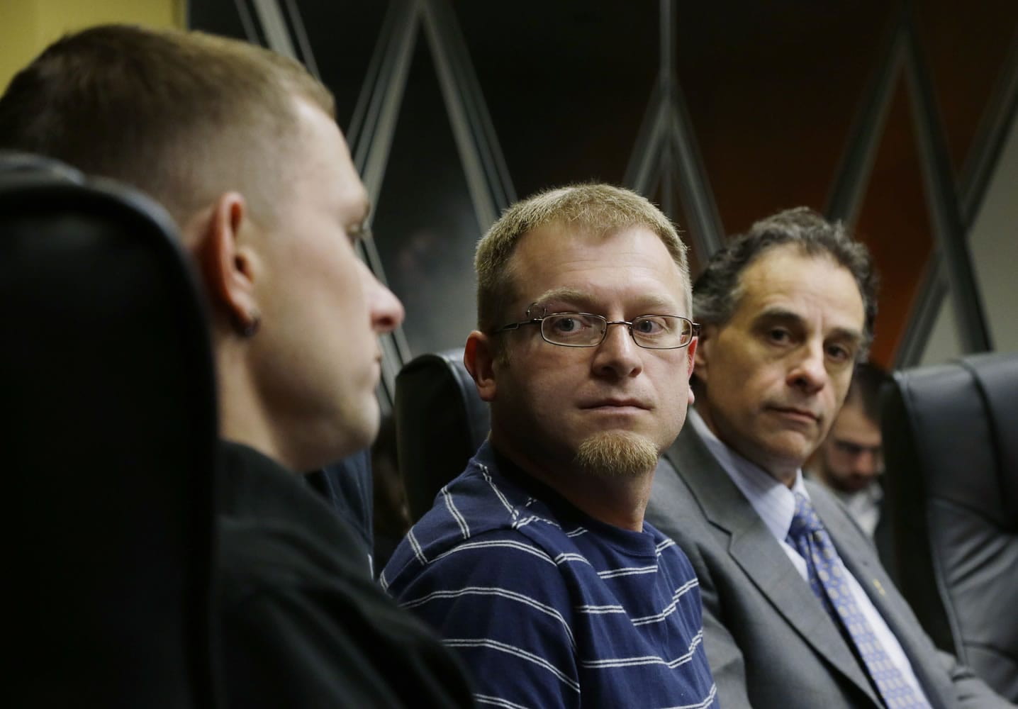 Eli Hall, center, looks on as his husband, Michael Hall, left, talks to reporters Tuesday  in Seattle.