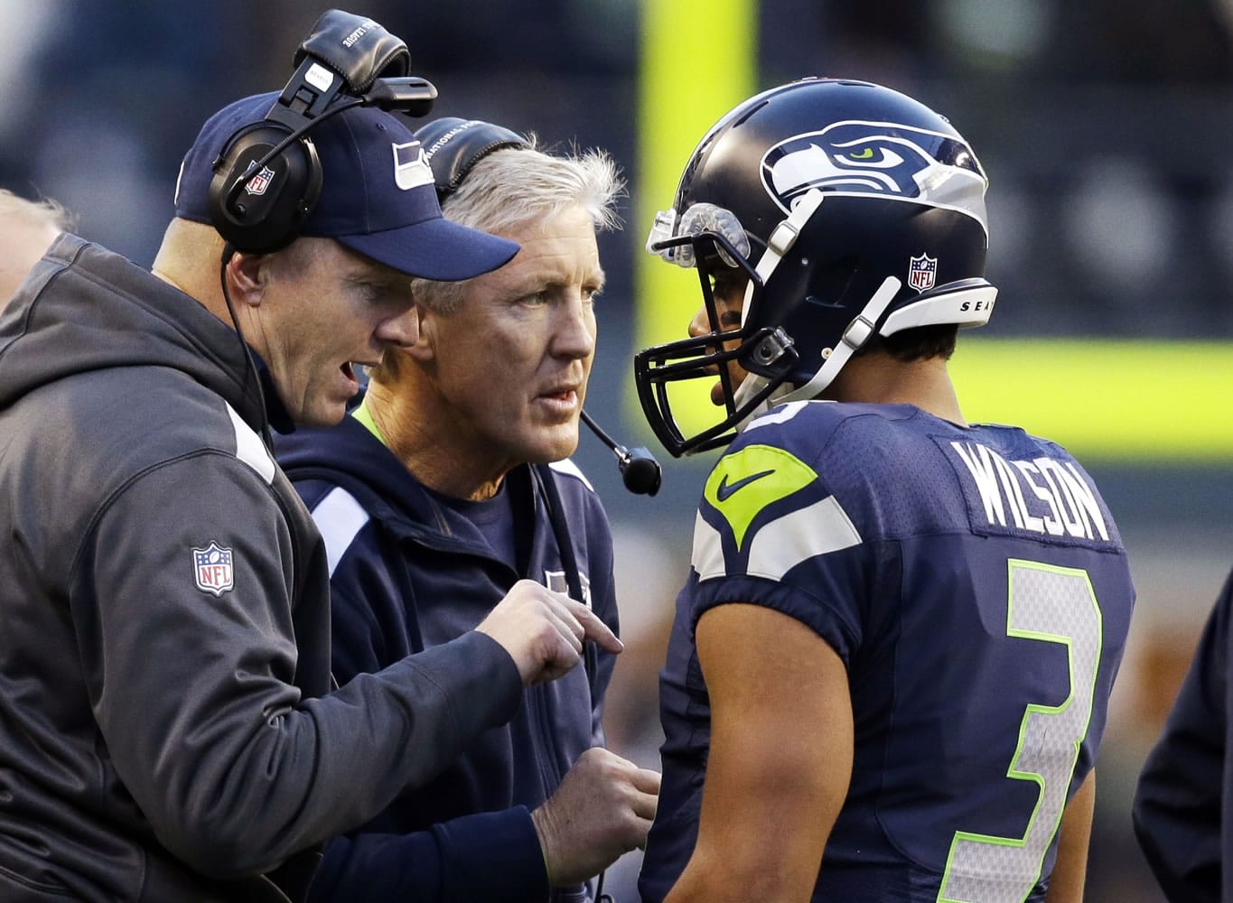 Seattle Seahawks quarterback Russell Wilson (3) talks with head coach Pete Carroll, center, and offensive coordinator Darrell Bevell before Wilson's final play against the Tampa Bay Buccaneers in overtime in an NFL football game Sunday, Nov. 3, 2013, in Seattle. The Seahawks won 27-24 on a field goal in overtime.