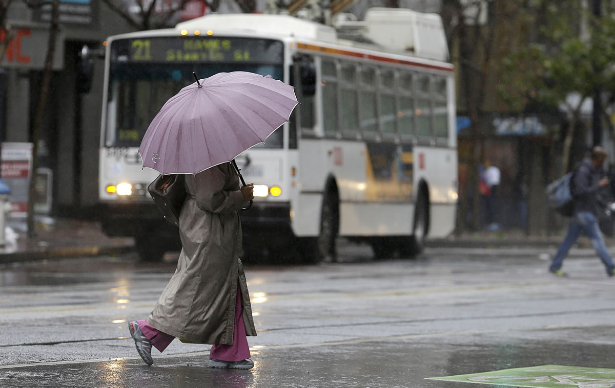 A woman carries an umbrella as she crosses Market Street in San Francisco, Saturday.