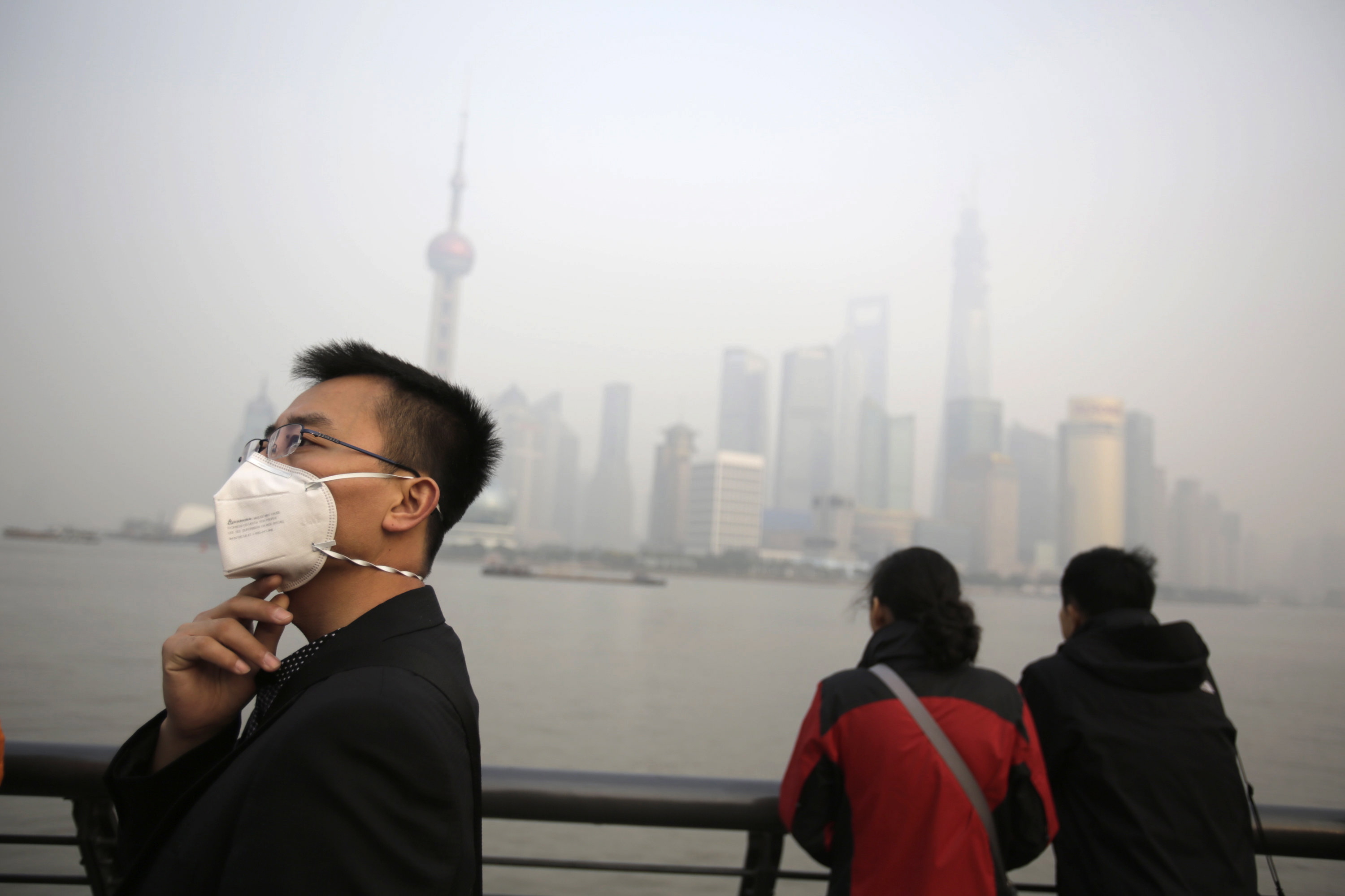 A tourist wearing a protective mask stands by as a couple look across the Huangpu River, shrouded in heavy haze Friday at the Bund in Shanghai, China.