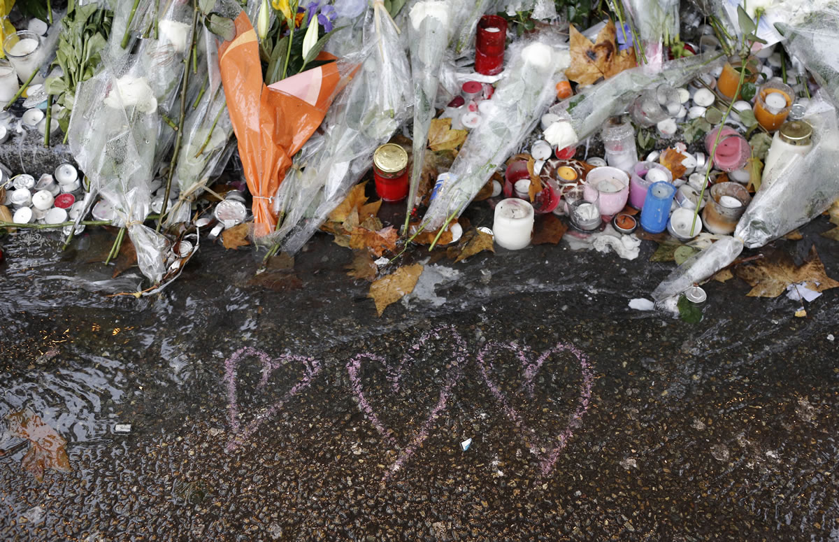 Hearts drawn and flowers lay on the pavement at a bar where an attack took place last week, Friday  on, Friday, Nov. 20, 2015 in Paris. old rain extinguished the flickering candles and drenched the packets of flowers outside the Paris attacks sites Friday, but people came anyway  to pay tribute, to mourn, to reflect on their city's losses one week later.