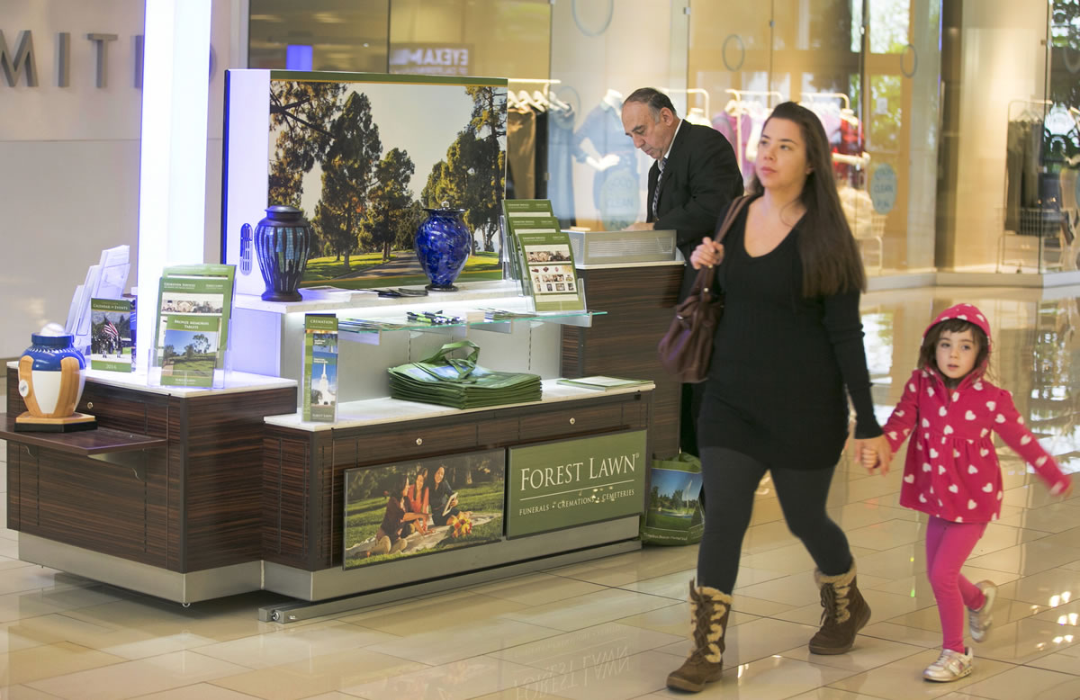 Shoppers walk past the Forest Lawn kiosk at the Glendale Galleria mall in Glendale, Calif.