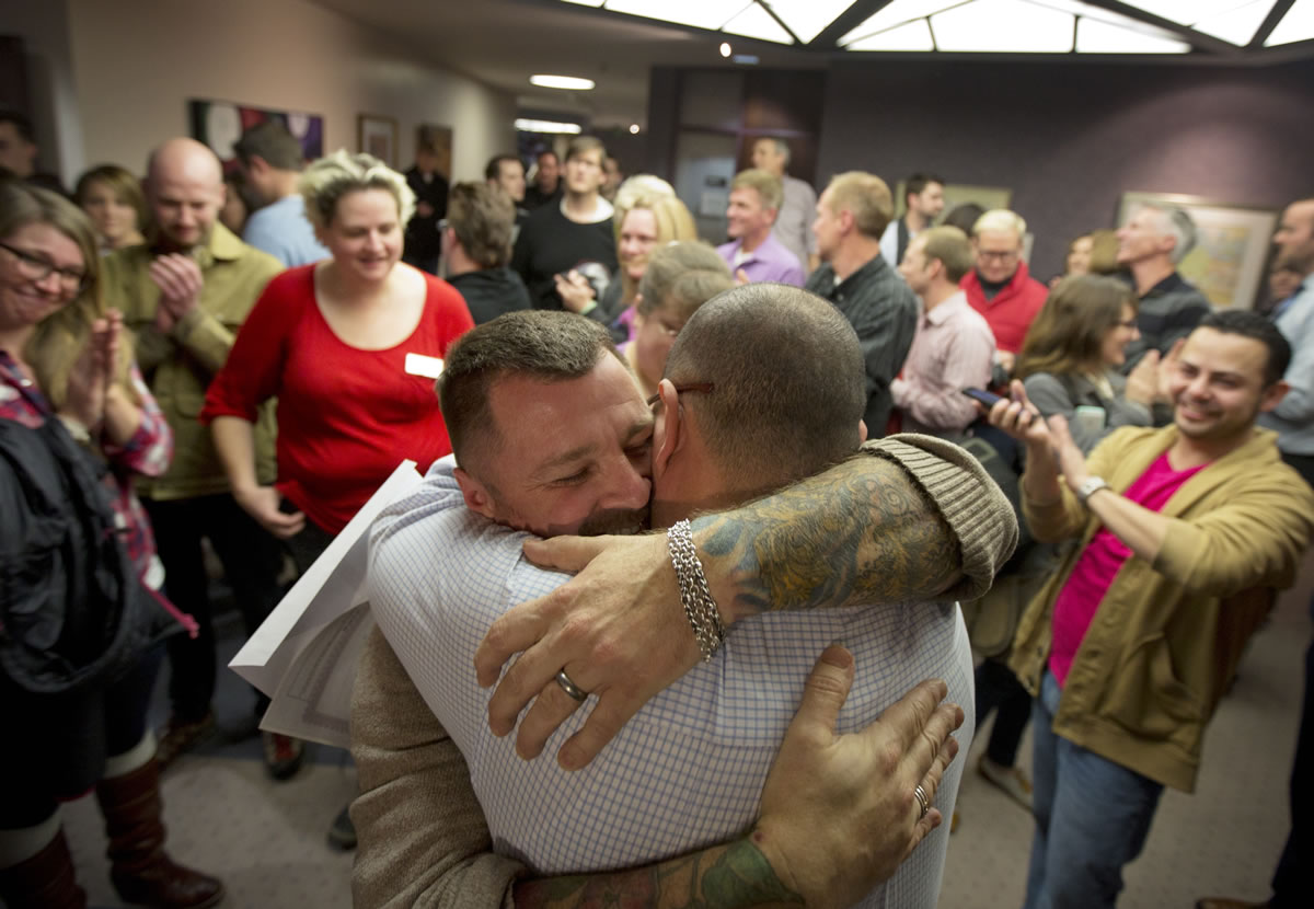 Chris Serrano, left, and Clifton Webb embrace after being married as people wait in line to get licenses outside of the marriage division of the Salt Lake County Clerk's Office in Salt Lake City.
