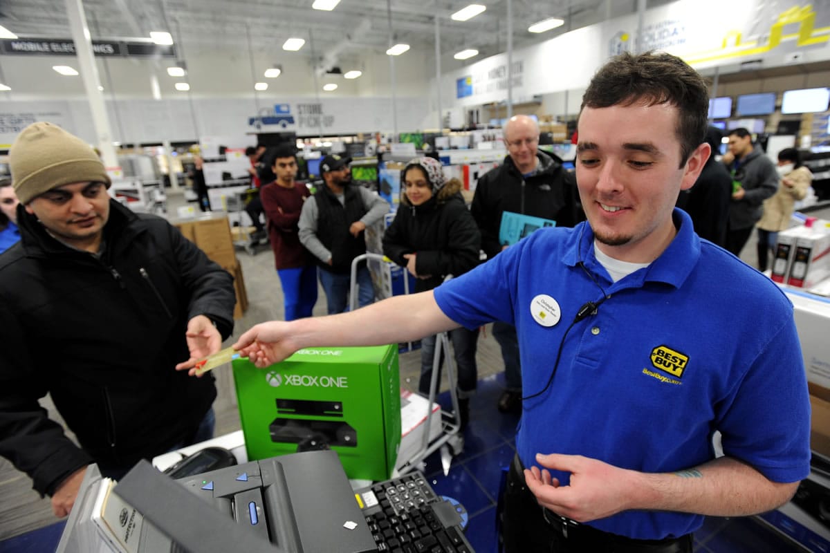 Just after midnight, Best Buy employee Christopher Gervais, right, hands back a credit card after he rang up a $499.99 Xbox One game set that is a doorbuster special at the electronics retailer on Black Friday in Dunwoody, Ga.