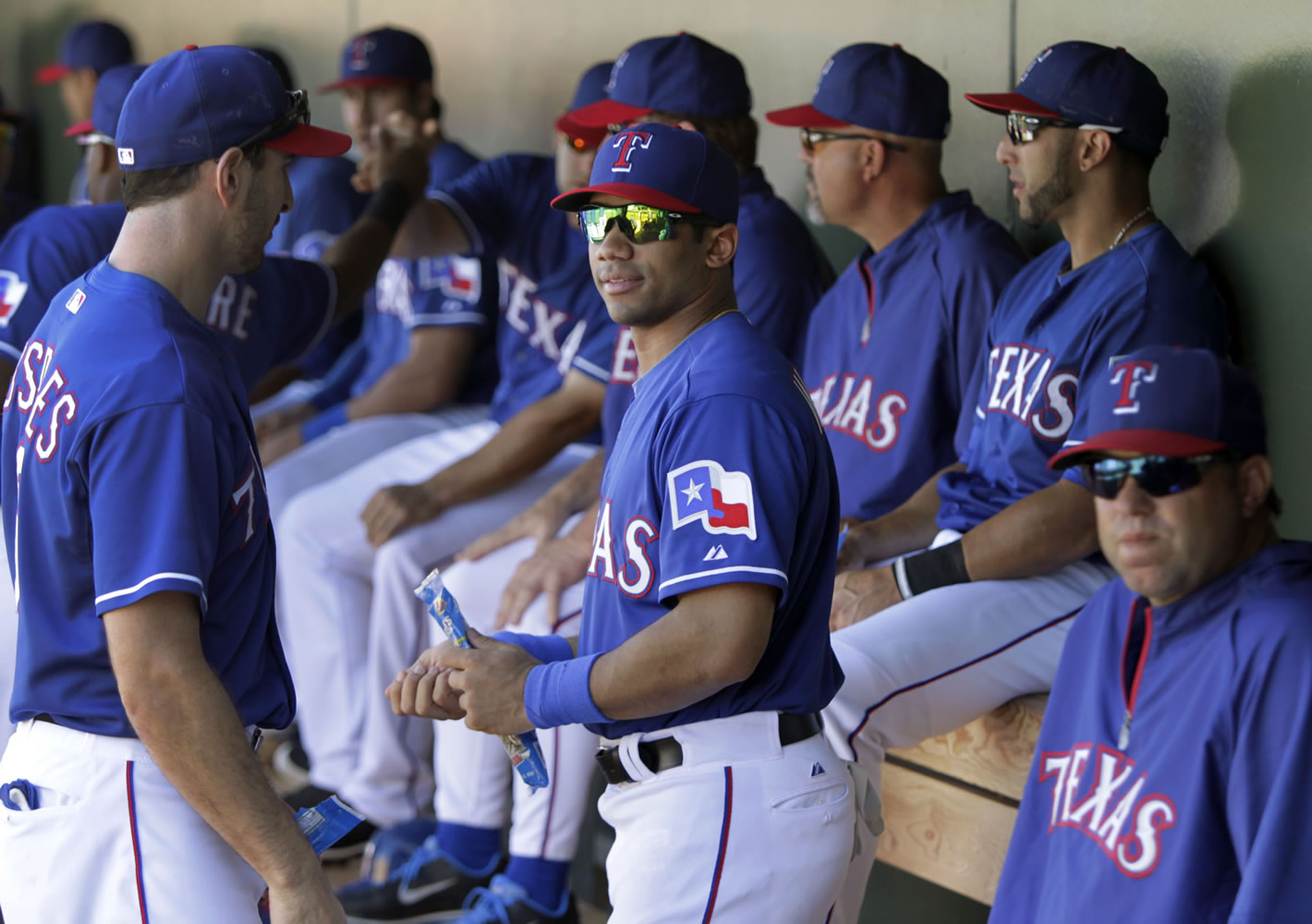 Seattle Seahawks quarterback Russell Wilson, center, talks with Texas Rangers' Adam Rosales, left, as he stands in the dugout during a spring training game against the Cleveland Indians on Monday in Surprise , Ariz.