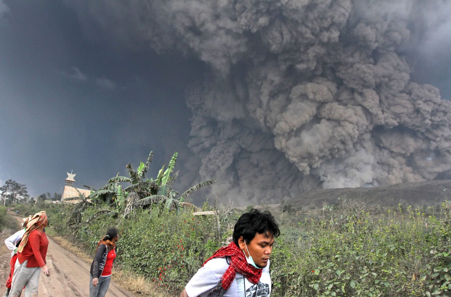 Associated Press
Villagers and a journalist prepare to flee as Mount Sinabung releases pyroclastic flows Saturday during an eruption that began four months ago in Namantaran, North Sumatra, western Indonesia. The rumbling volcano has unleashed fresh clouds of searing gas, killing at least 14 people and injuring more; the tolls are expected to rise.