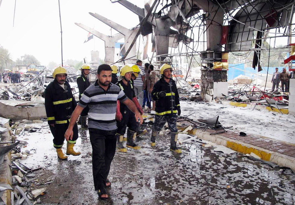 Firefighters and civilians inspect the site of a massive bomb attack in Hillah, about 60 miles south of Baghdad on Sunday.