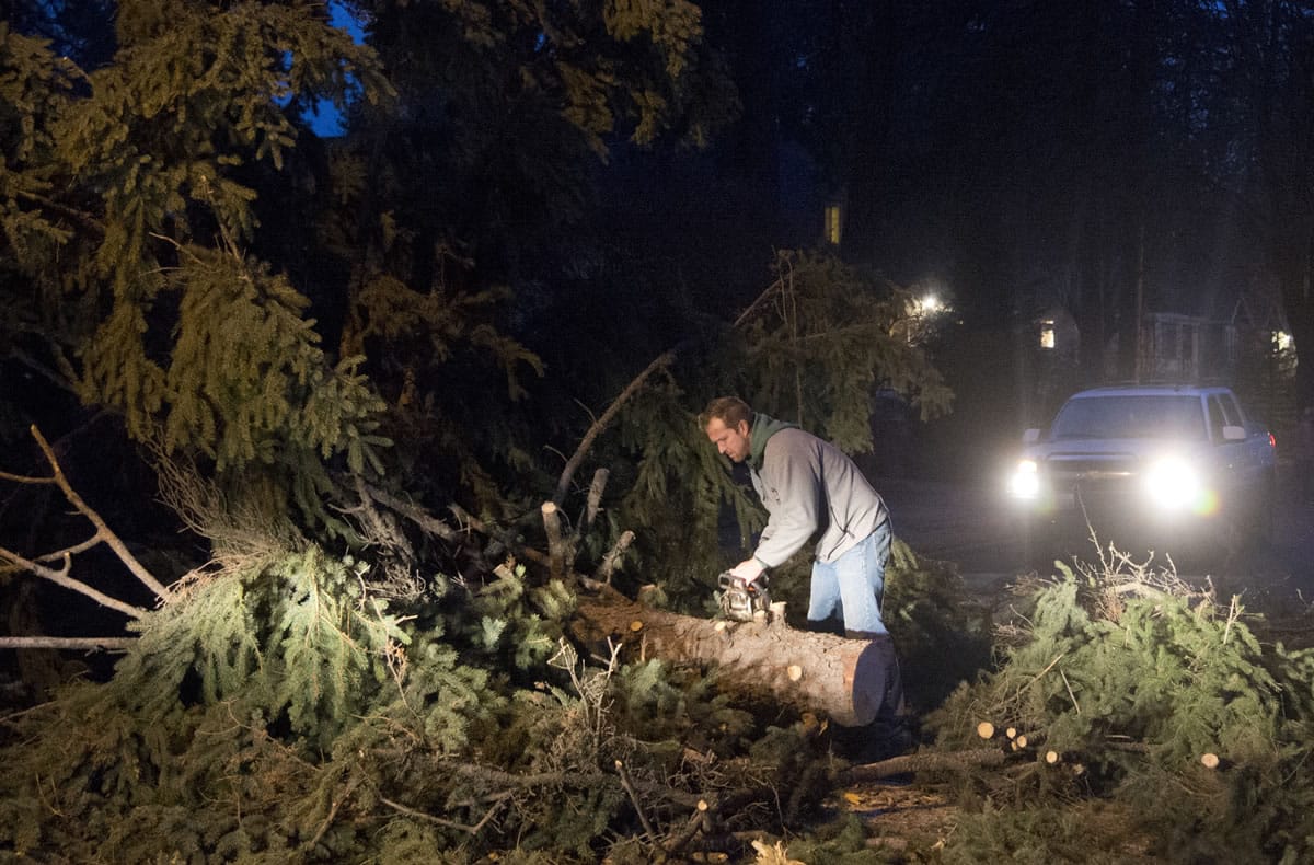 Cameron Napora, a contractor, stops to cut a large tree that was blocking the road during a windstorm that swept through Spokane on Tuesday. Rain and high winds snarled traffic and knocked out power to tens of thousands of people in Western Washington on Tuesday.
