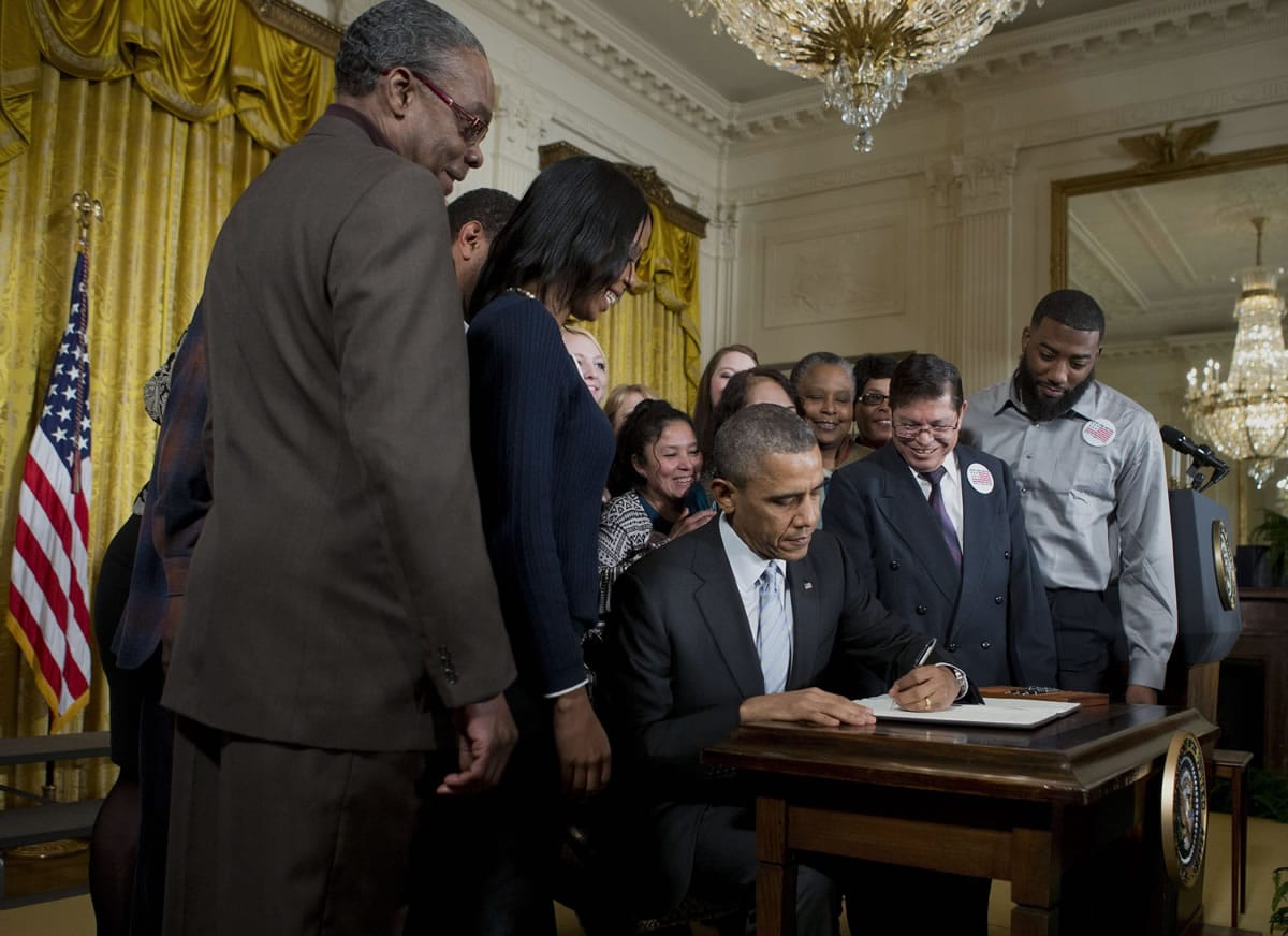 President Barack Obama, surrounded by workers, Wednesday signs an executive order to raise the minimum wage for federal contract workers during a ceremony in the East Room of the White House in Washington.