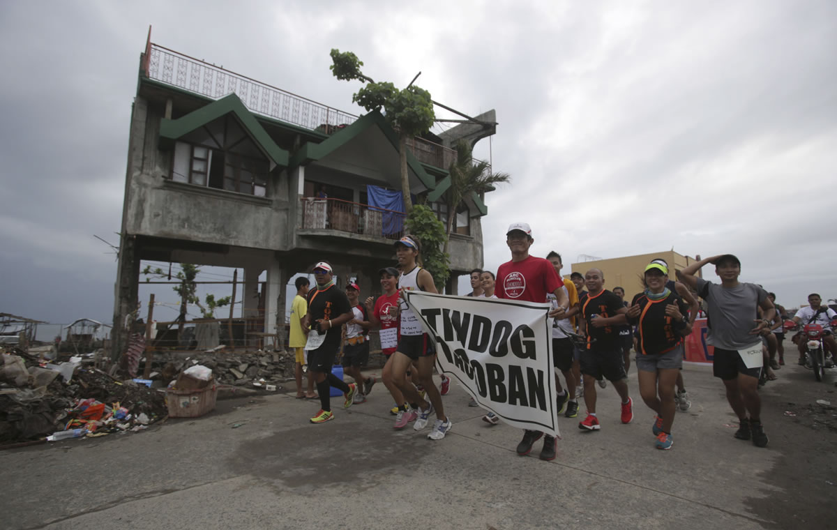 Typhoon survivors in Tacloban, Philippines, run Sunday with a poster reading &quot;Rise up Tacloban&quot; to show their support for fellow survivors and the city of Tacloban.