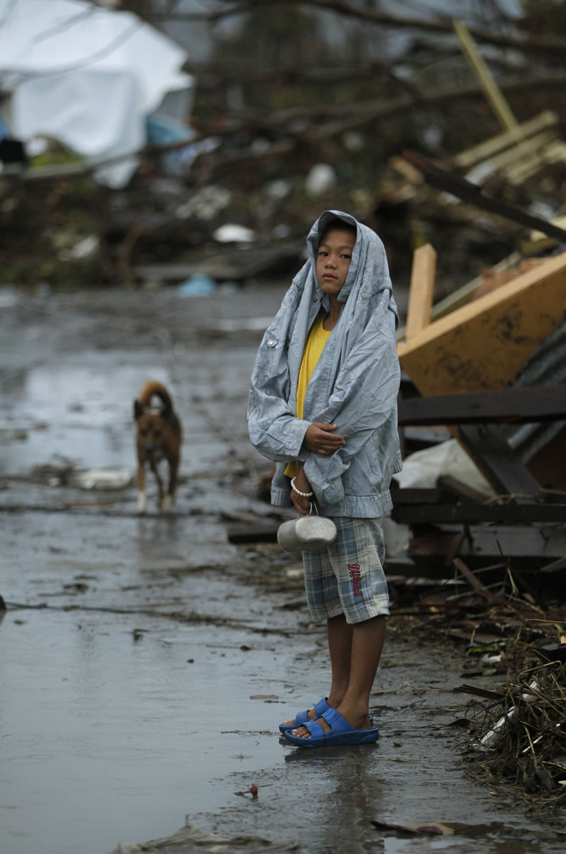 A young boy waits at the side of the road for fresh water surrounded by debris from Typhoon Haiyan in Tacloban, central Philippines, today.