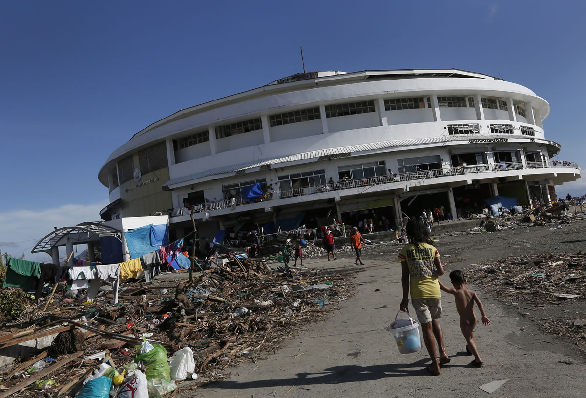 A young girl walks her brother to the Tacloban City Convention Center known as the Astrodome Thursday where hundreds of displaced typhoon survivors have set up makeshift shelters throughout the complex's once bustling shops and popular basketball court.