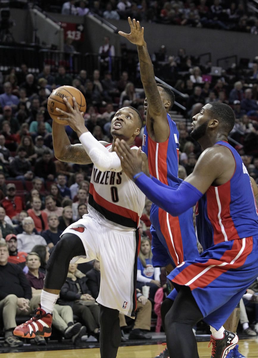 Portland Trail Blazers guard Damian Lillard, left, goes to the basket against the Detroit Pistons' Andre Drummond, right, and Brandon Jennings during the second half Monday.