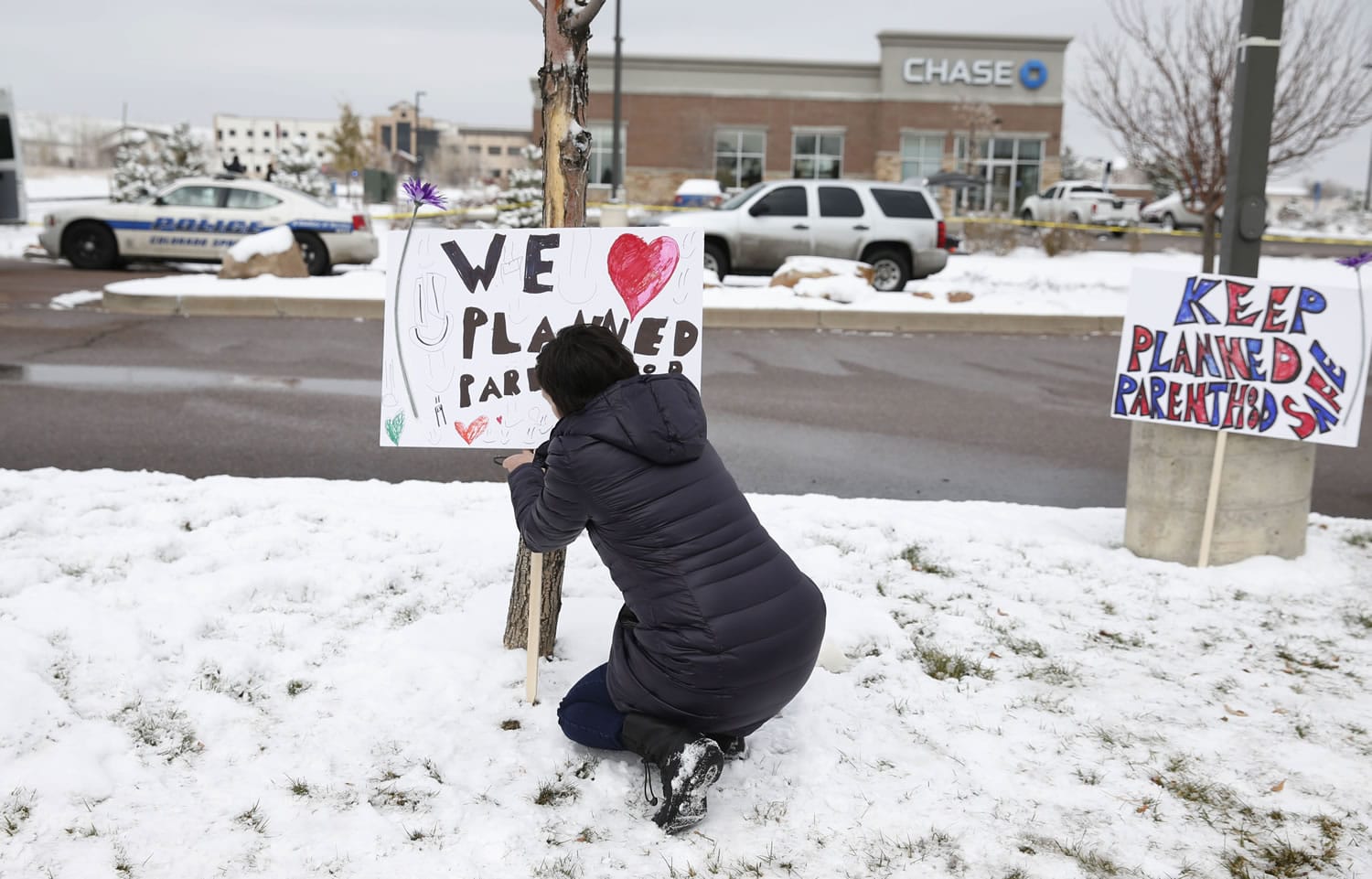 Bethany Winder, a nurse who lives in Colorado Springs, Colo., plants a sign in support of Planned Parenthood just south of its clinic as police investigators gather evidence near the scene of Friday's shooting at the clinic Sunday, Nov. 29, 2015, in northwest Colorado Springs.