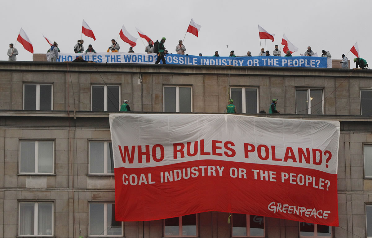 Climate activists with protest banners wave Polish flags on the rooftop of the Economy Ministry in Warsaw, Poland on Monday. They went up the rooftop to protest a coal conference opening to coincide with U.N.