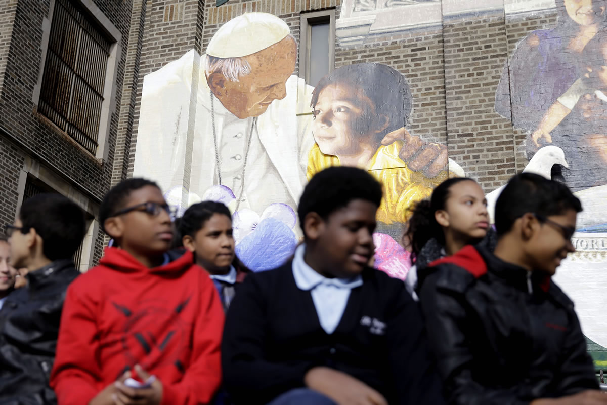 Students sit beneath an image of Pope Francis during a ceremony dedicating the City of Philadelphia Mural Arts Program?s mural, titled The Sacred Now: Faith and Family in the 21st Century on Monday in Philadelphia.(AP Photo/Matt Rourke)