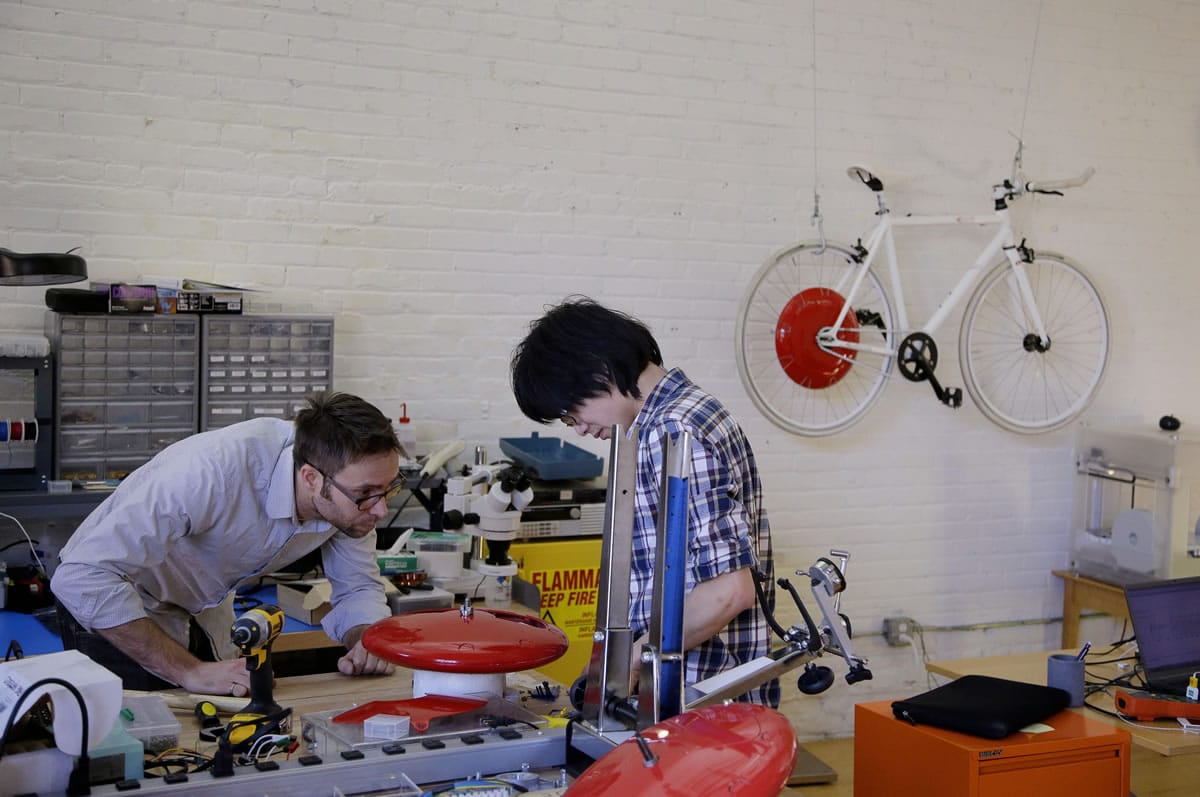 Mechanical and software engineer Julian Fong, right, and vehicle design engineer Jon Stevens work on a development to the Copenhagen Wheel, red disk, a human/electric hybrid bicycle engine at Superpedestrian in Cambridge, Mass.
