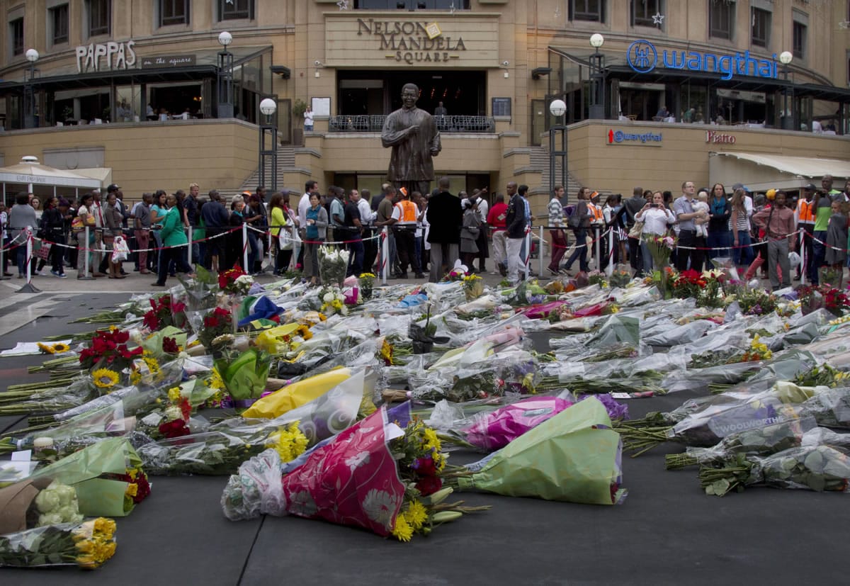 Floral tributes to former president Nelson Mandela pile up beneath his statue Friday on Mandela Square in Johannesburg. Mandela died Thursday at his Johannesburg home after a long illness.