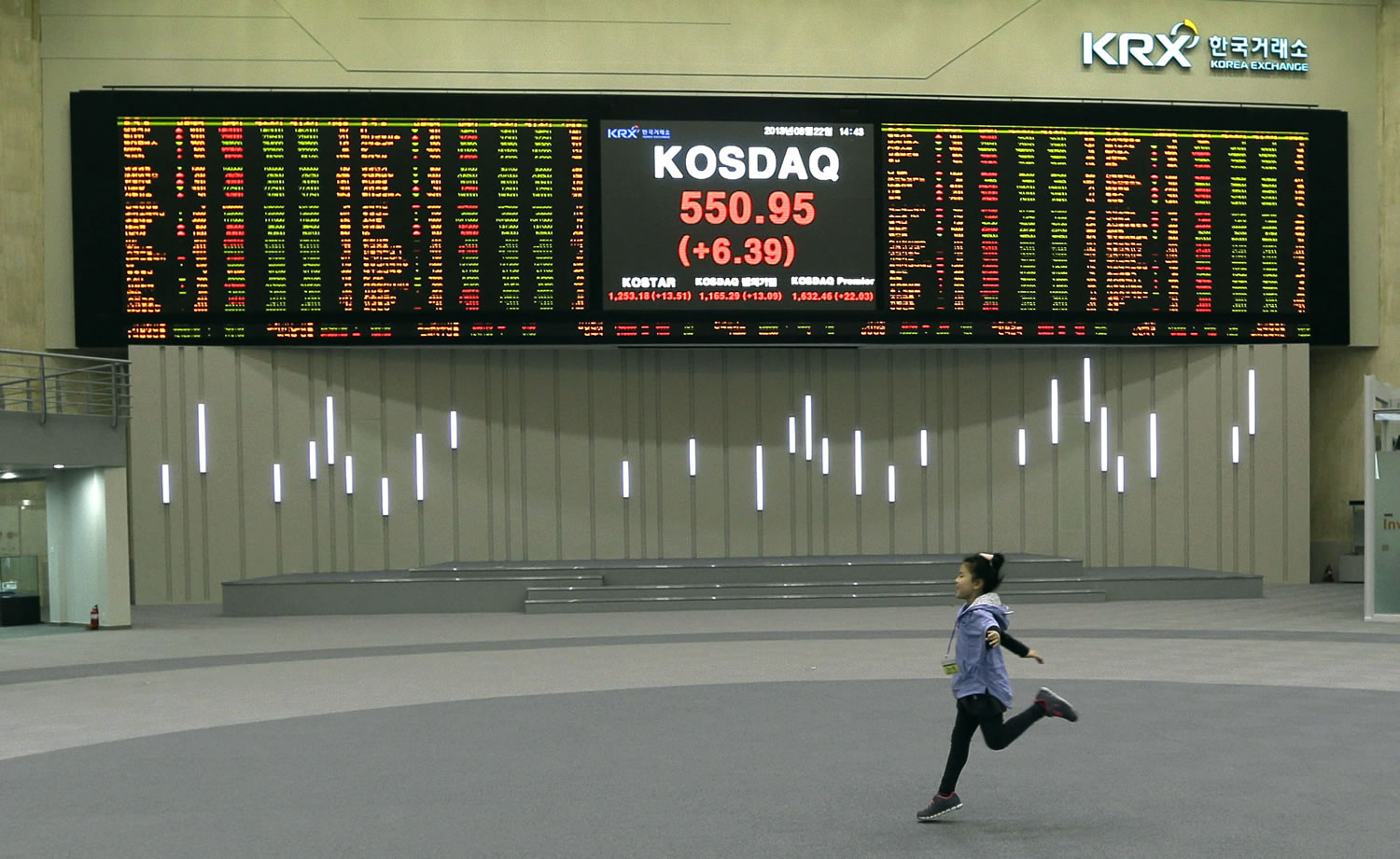 A girl plays near a screen showing the stock prices at the Korea Exchange in Seoul, South Korea.