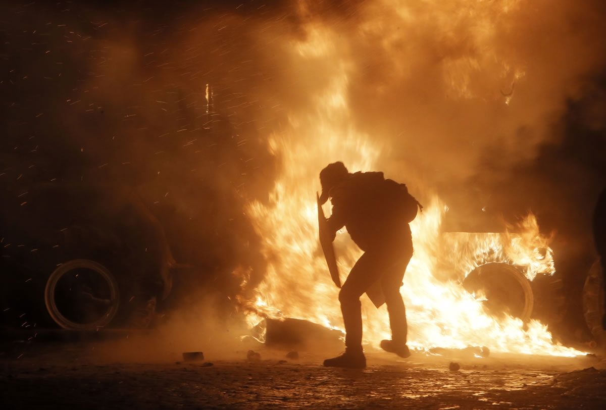 A protester throws a Molotov cocktail toward a burning police car during clashes with police, in central Kiev, Ukraine, early today.