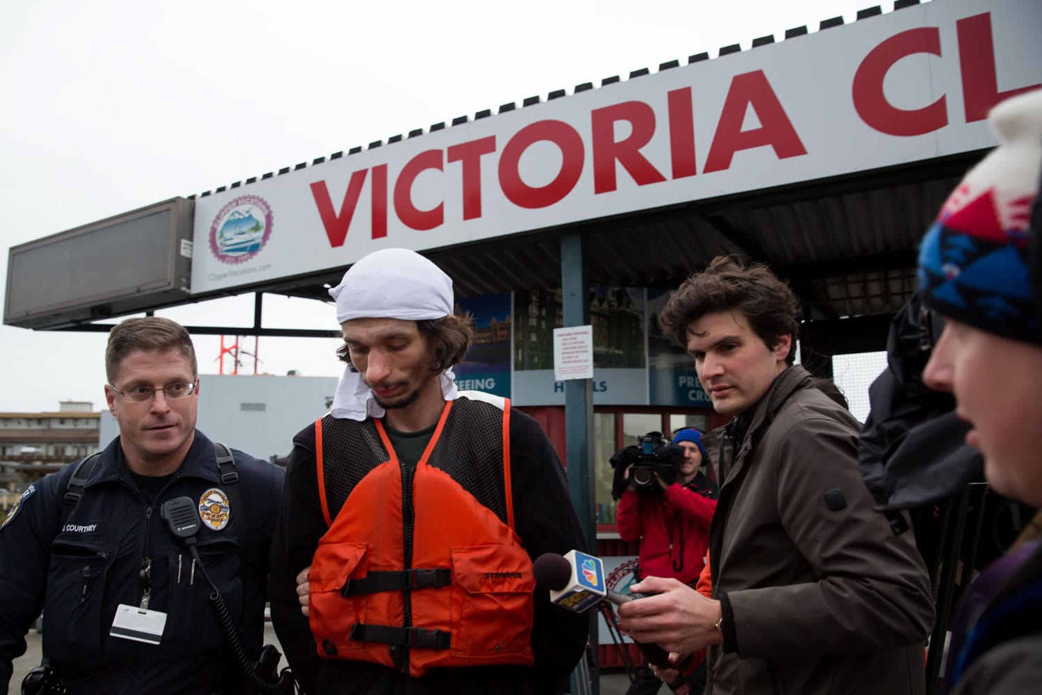 A police officer escorts an apprehended suspect, wearing a white cloth on his head, who allegedly commandeered the Victoria Clipper after it was found adrift in Elliot Bay in Seattle on Sunday