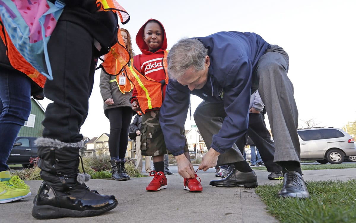 Gov. Jay Inslee, right, ties the shoe of kindergartner Darius Richardson as Inslee escorts elementary school students on a &quot;walking school bus&quot; Tuesday morning in Seattle.