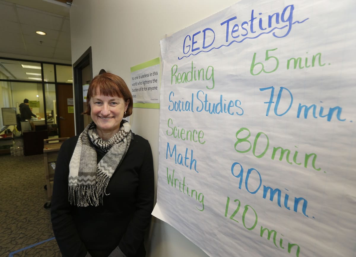 Sally Raftery, program coordinator and GED examiner at Bellevue College, stands next to a sign in the college's testing center in Bellevue that tells how long each section of the Washington state GED test takes to complete.