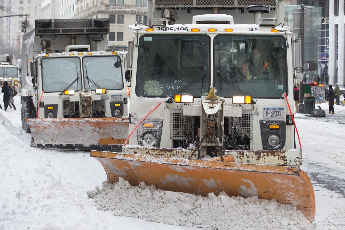 Sanitation trucks outfitted with snow plows clear Fifth Avenue of snow Friday in New York.