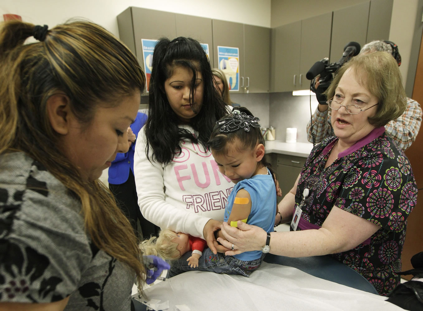 Nurses Fatima Guillen, left, and Fran Wendt, right, give Kimberly Magdeleno, 4, a Tdap whooping cough booster shot as she is held by her mother, Claudia Solorio, on May 3 at a health clinic in Tacoma.