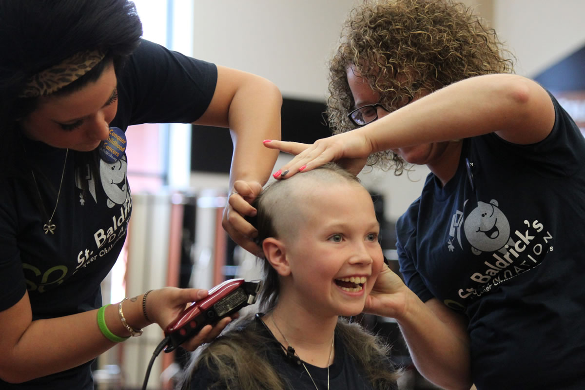 Washougal third-grader and cancer survivor Sammy Mederos reacts to getting her long locks of curly blond hair shaved off by Shelby Cummings (left) and Holly Thorpe (right) during a fundraiser for the St. Baldrick's Foundation Sunday at Washougal High School. Mederos was diagnosed with leukemia when she was in kindergarten. Now cancer-free, she and her parents, Michele and Dennis Mederos, helped organize the event.