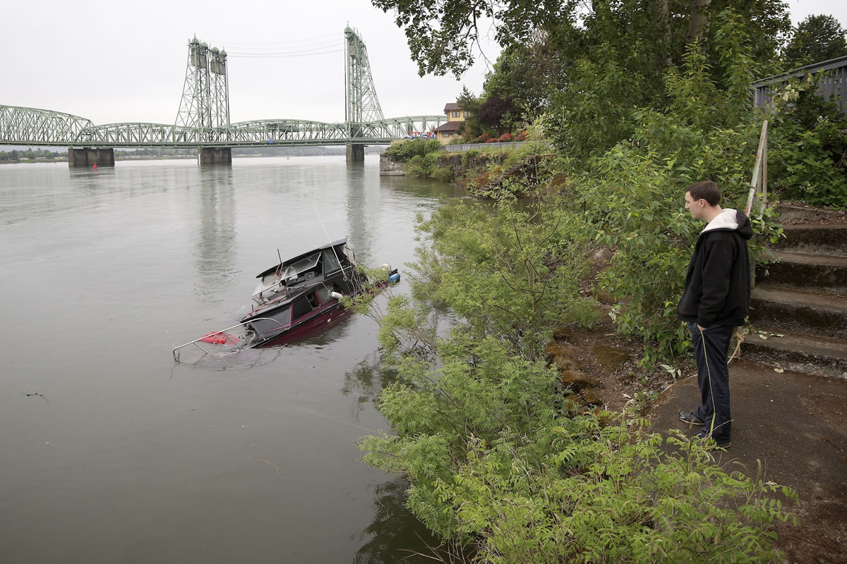 Michael Cole of Vancouver stops to look at a partially submerged boat. The boat has remained at the shoreline of Waterfront Park for more than a month.