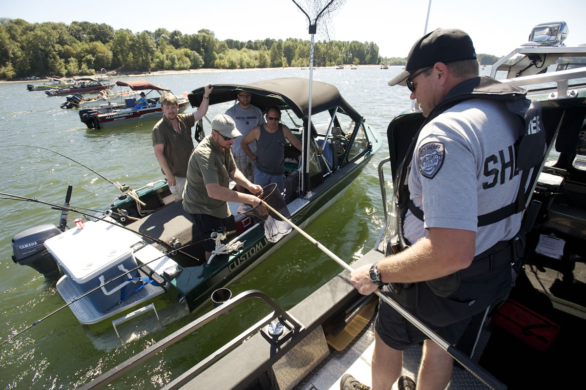 Todd Baker of the Clark County Sheriff's Office marine patrol hands paperwork back to a boat of anglers anchored near the shipping channel at the mouth of the Lewis River.