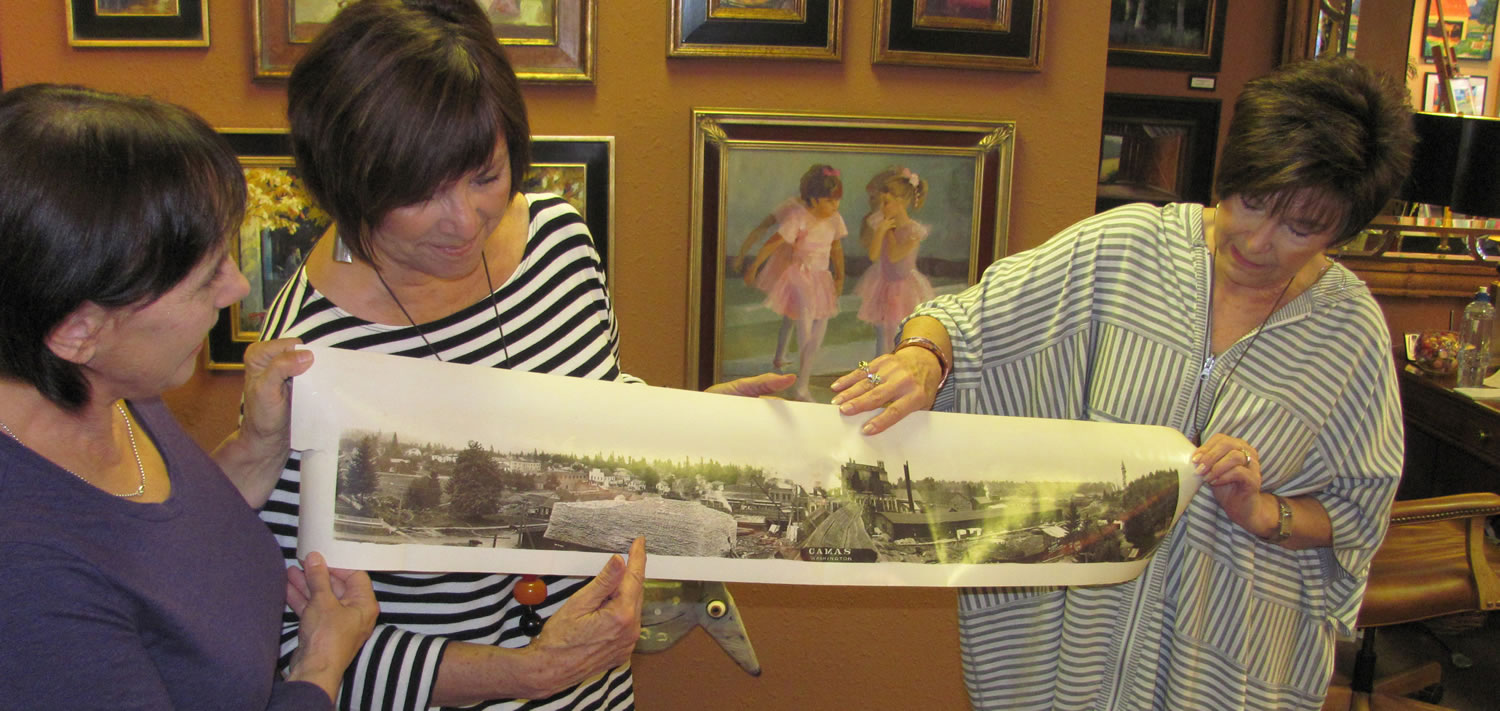 Artist Maria Repetto and downtown Camas art gallery owners Sharon Ballard and Marquita Call (left to right) hold the photograph that is the inspiration for the first mural that will be part of the Camas-Washougal Mural Project. The image of downtown Camas was taken in 1911 or 1912 from Northwest Sixth Avenue and Division Street, according to the picture's owner Brent Erickson. The mural will be painted by Repetto and mounted on a 3 foot by 30 foot space above the entry to the Ballard &amp; Call Fine Art Gallery.