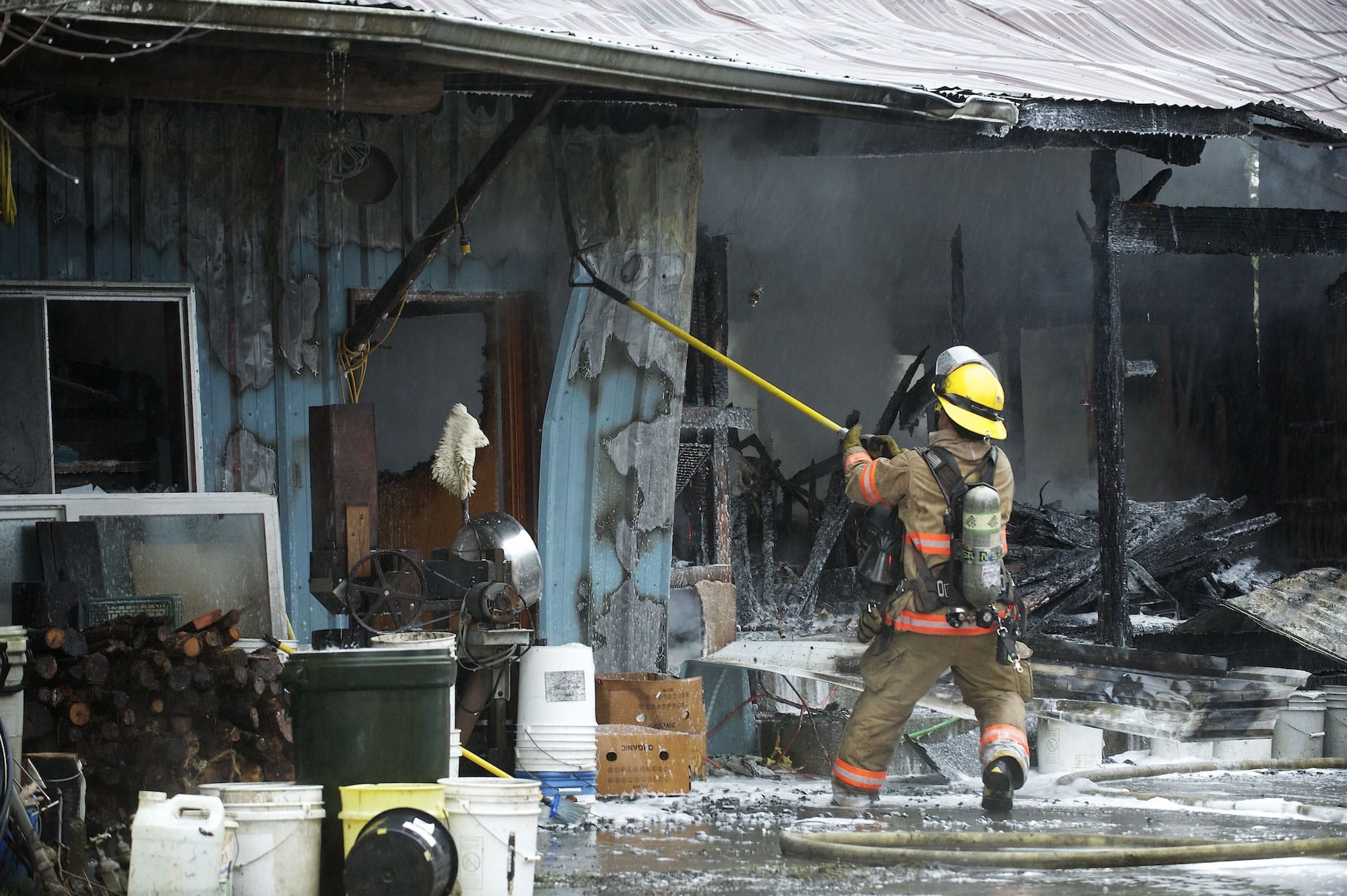 A firefighter pulls metal siding from the shop at the John and Delores Matson residence in Hockinson on Wednesday morning.