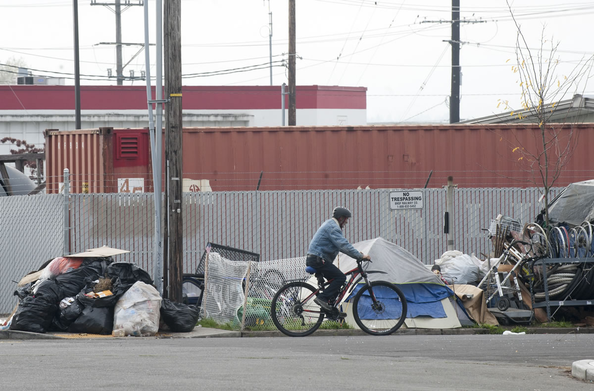 Oct. 21: A man cycles on a street next to a large pile of garbage and tents where homeless people used to live near Share House in downtown Vancouver.