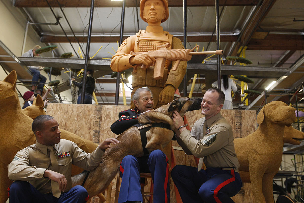 Retired U.S. Marine Robert Harr, 86, middle, a World War II dog trainer, sits Thursday with U.S. Marine Cpl. Juan Rodriguez, left, U.S. Marine Gunnery Sgt. Christopher Willingham and Lucca on Natural Balance Pet Foods' 2013 Rose Parade float, &quot;Canines with Courage&quot; in Irwindale, Calif. The float is a floral replica of the Military Working Dog Teams National Monument being constructed in San Antonio, Texas. Lucca, an 8-year-old German Shepherd-malinois mix, was deployed in Iraq and Afghanistan. After losing a leg to a roadside bomb, Lucca is now retired and lives with her first handler, Sgt.