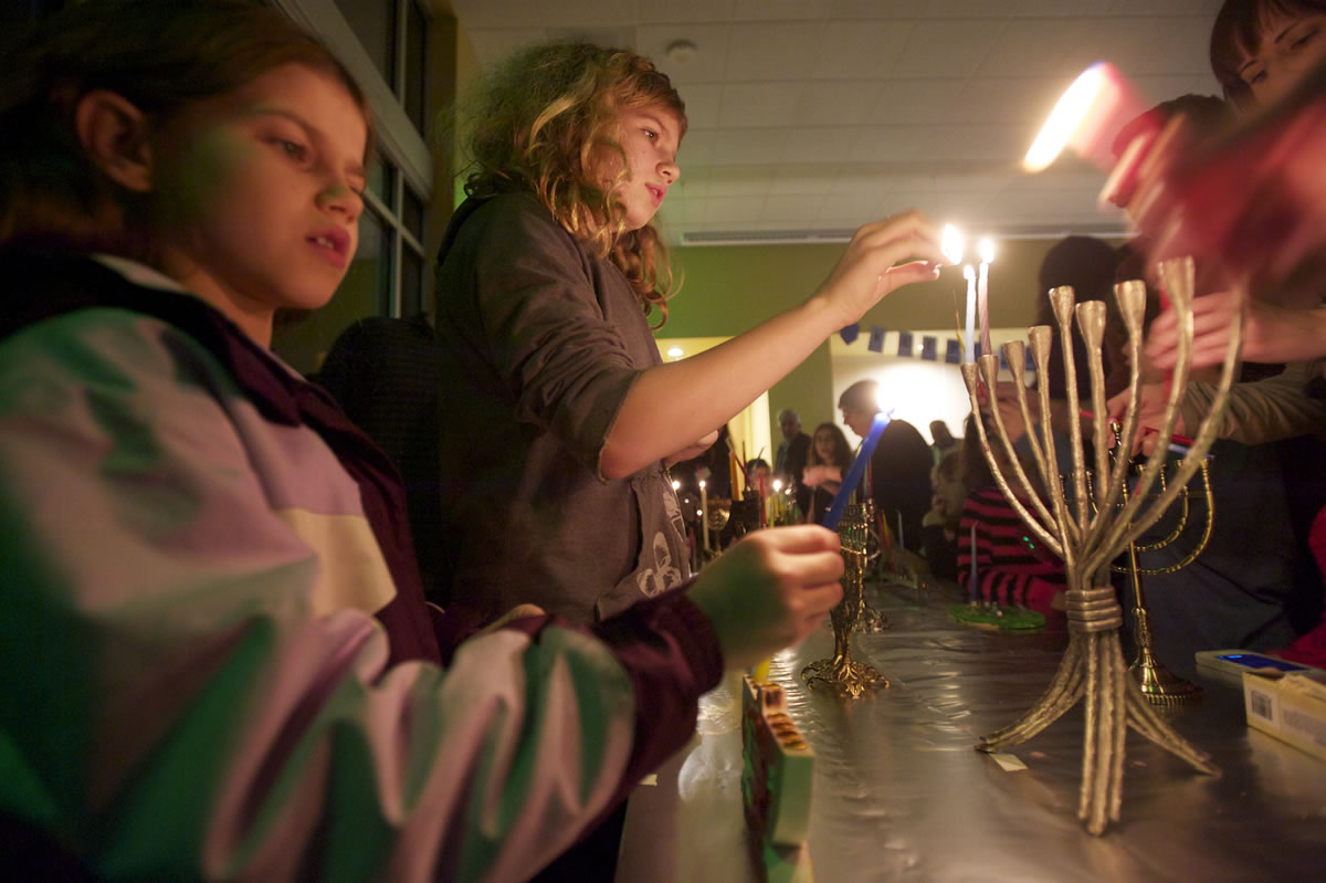 Sisters Bailey VanRoy-Amundson, left, and Anna VanRoy-Amundson, light menorahs at the Congregation Kol Ami Hanukkah party.