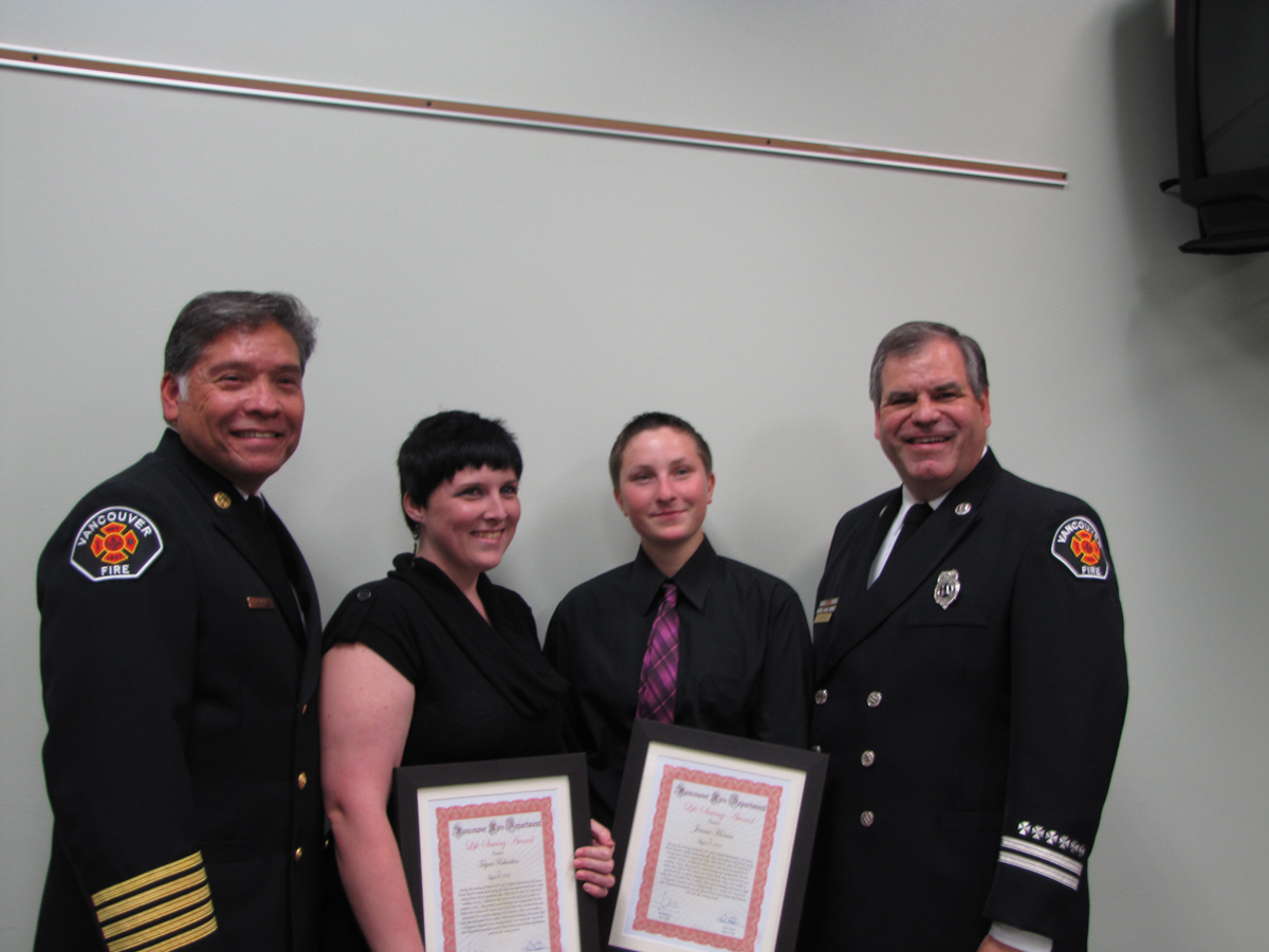 Talynia Richardson, center-left, and Jenna Horan pose with their Vancouver Fire Department Life-Saving certificates Tuesday evening. They are flanked by Vancouver Fire Chief Joe Molina, left, and Capt.