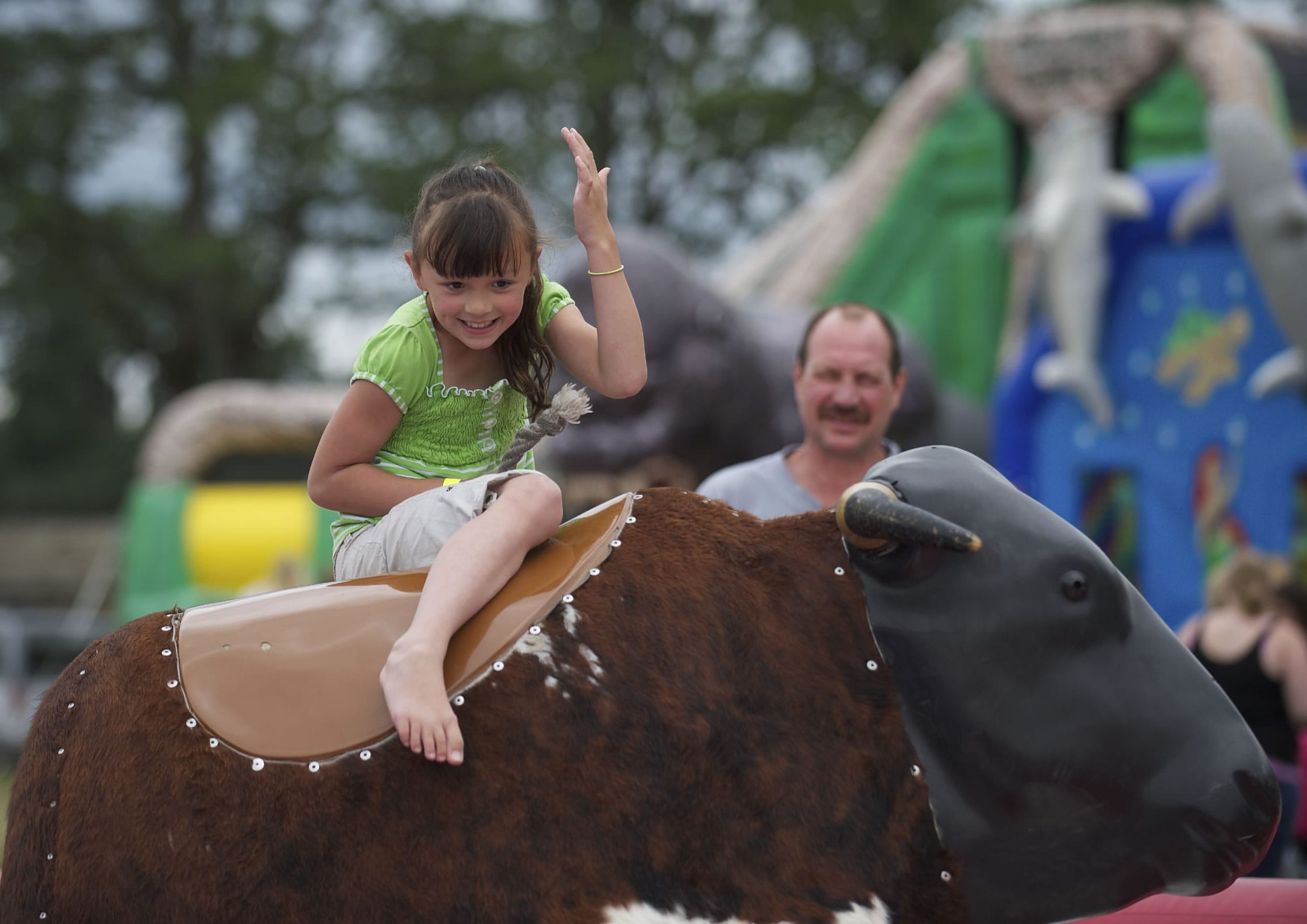 Talayna Dunaway, 7, of Battle Ground, does her best to stay atop a mechanical bull while her grandfather David Green watches from the background at Harvest Days in Battle Ground on Sunday July 22, 2012.