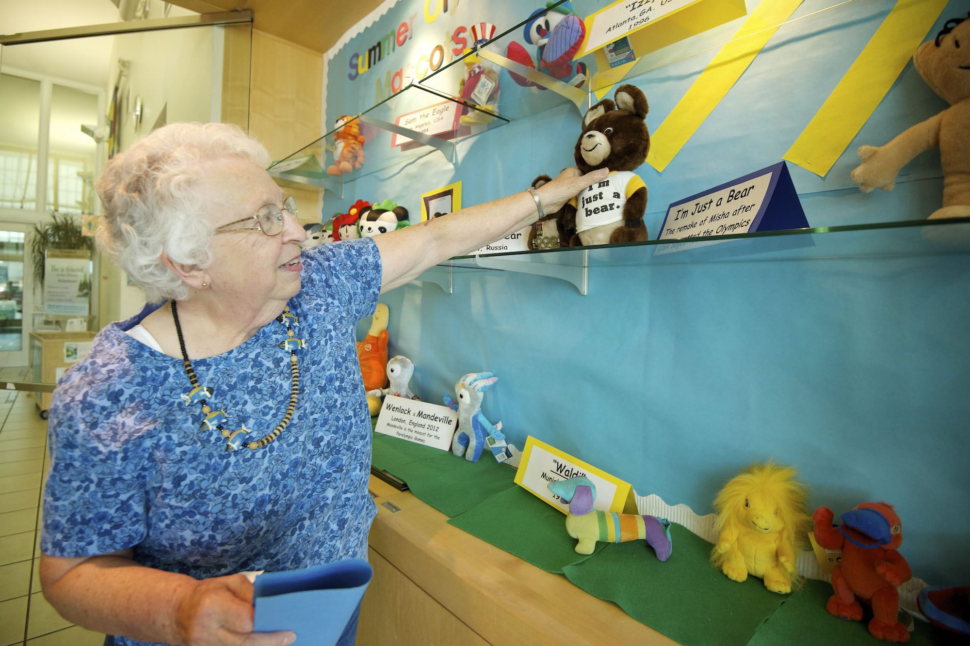 Rosalee Johnson adjusts her display of Olympic mascot plushies at Three Creeks Community Library.