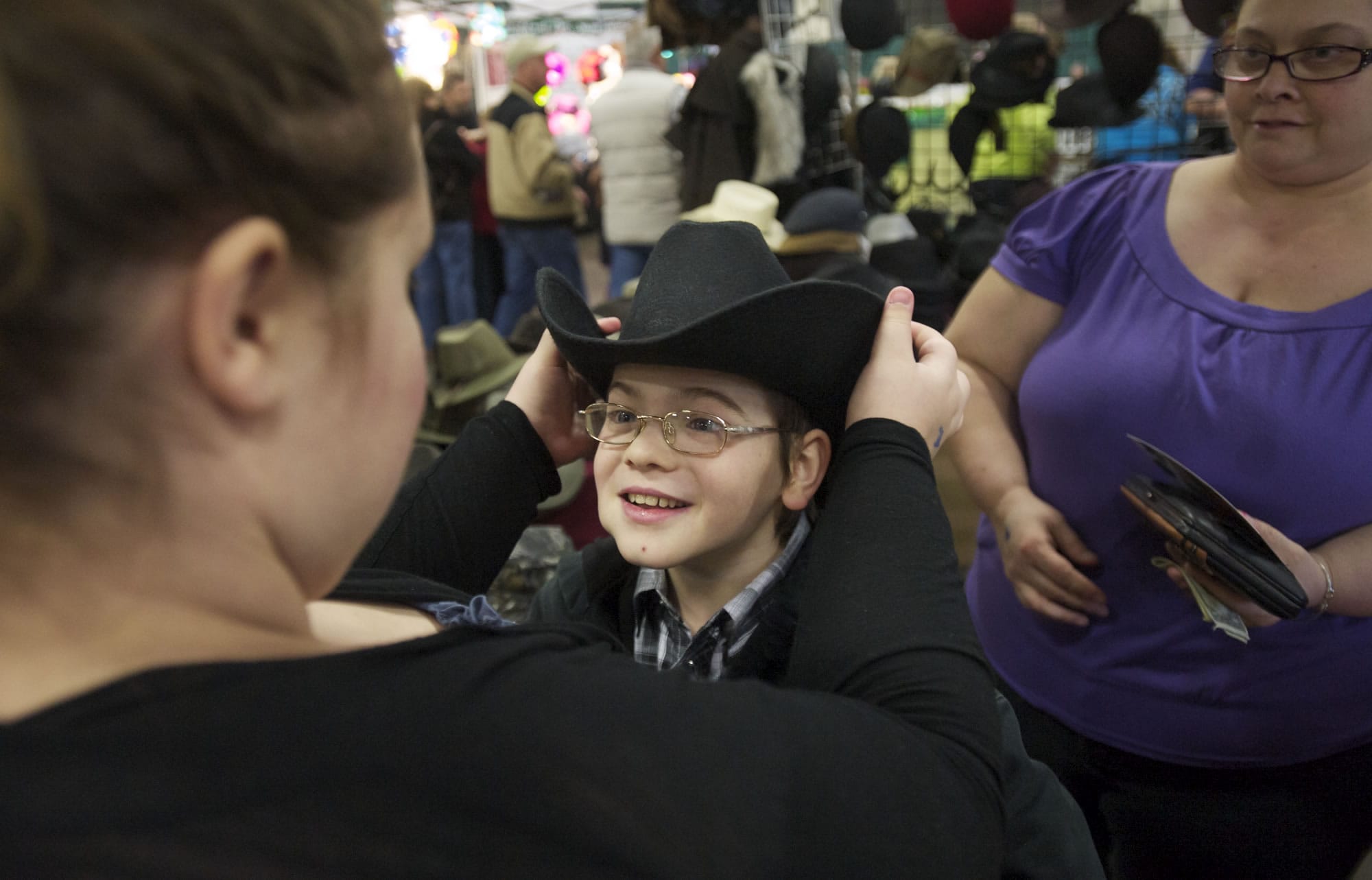 Austin Wiley, 10, picks out a new hat with help from his sister Mariah Wiley, left, and mom Kathy Romero at the Washington State Horse Expo on Sunday.