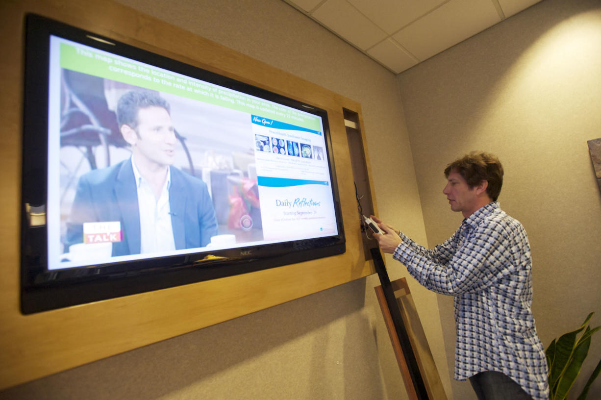 Randy Short of EcoDigital Media installs a digital display in the lobby of the Cancer Center at PeaceHealth Southwest Medical Center.