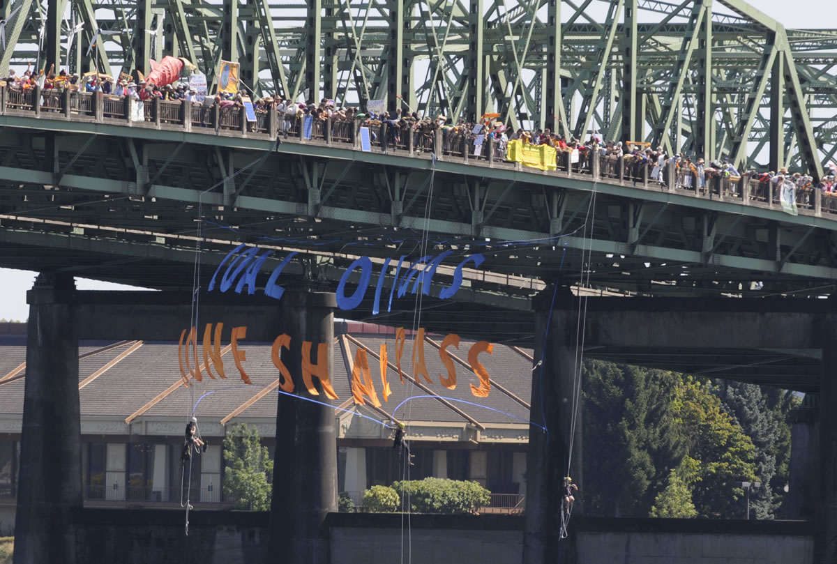 Three protesters on ropes lower a banner under the bridge supports as hundreds of protesters cross the Columbia River in support of an amphibious demonstration at the Interstate bridge against proposed fossil fuel facilities in the Northwest, in Vancouver, Wa., Saturday July 27, 2013.