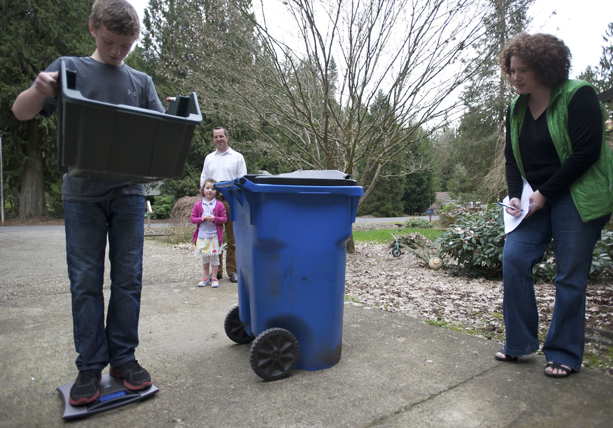 Eli Loudenback, 12, weighs his family's trash and recycling for the week while his mother, Amy, writes down the results at their Brush Prairie home this month. Eli's father, Robert, and 5-year-old sister, Romy, watch in the background.