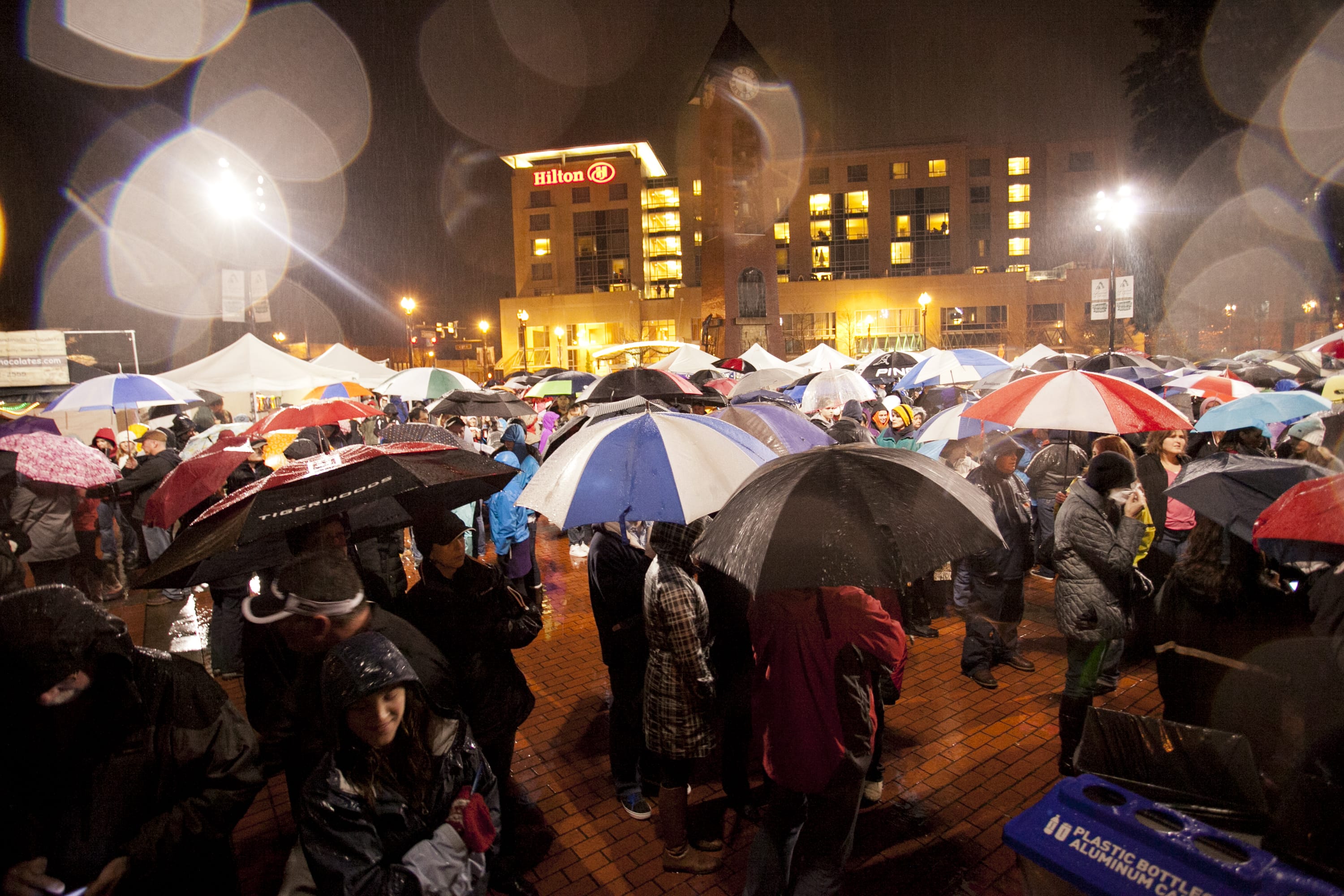 Crowds of people wearing raincoats and huddled under umbrellas attend the Vancouver Rotary Foundation's 17th annual community tree-lighting Friday evening at Esther Short Park.