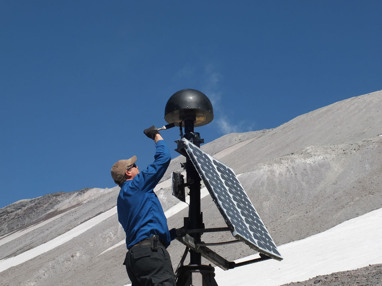 Cascades Volcano Observatory scientist Ben Pauk applies protective paint to a GPS antenna on Mount St. Helens.