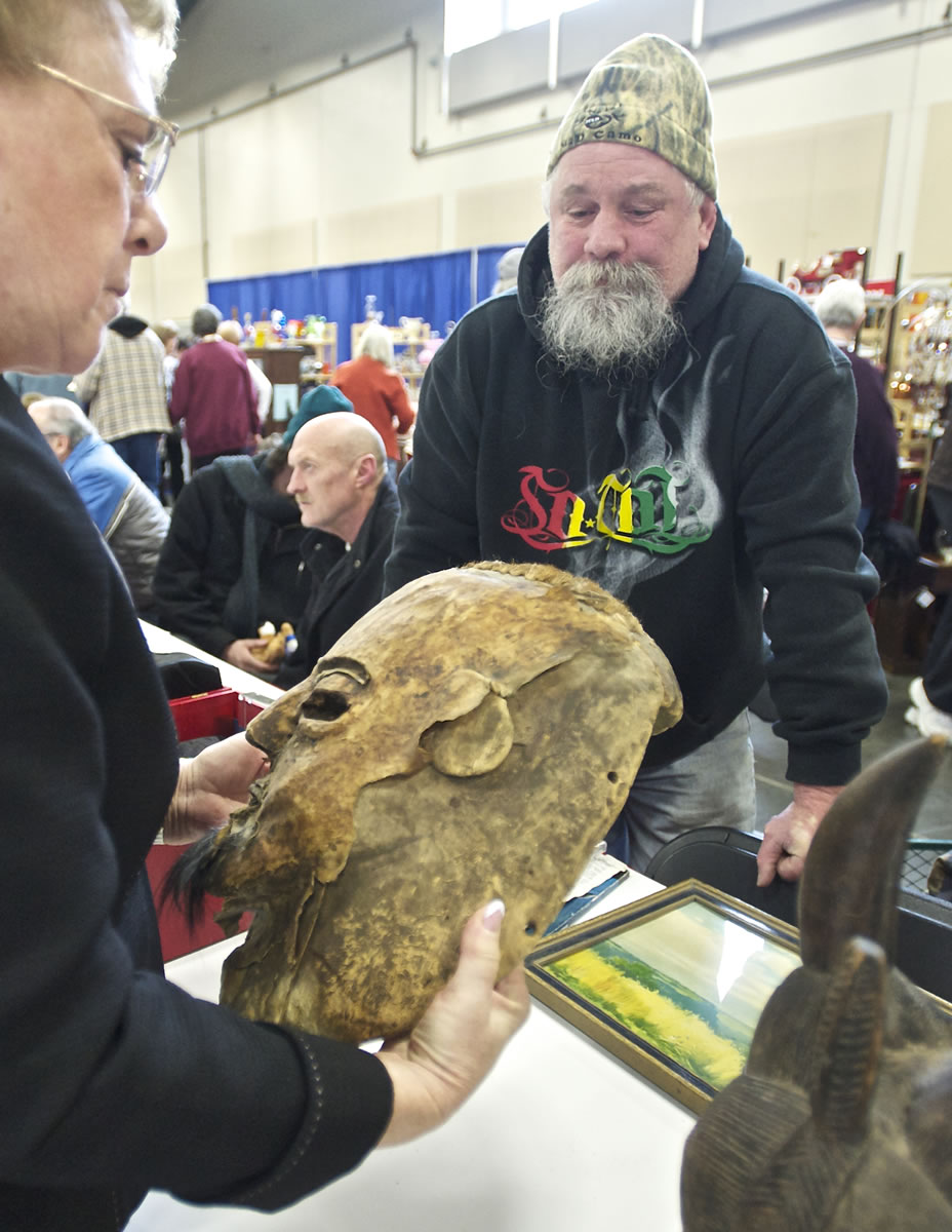 Mike Millspaugh, of Portland, has expert appraiser Kathleen Victor look on Saturday at a pair of wood-carved masks that he bought at an estate sale in Rogue River, Ore.