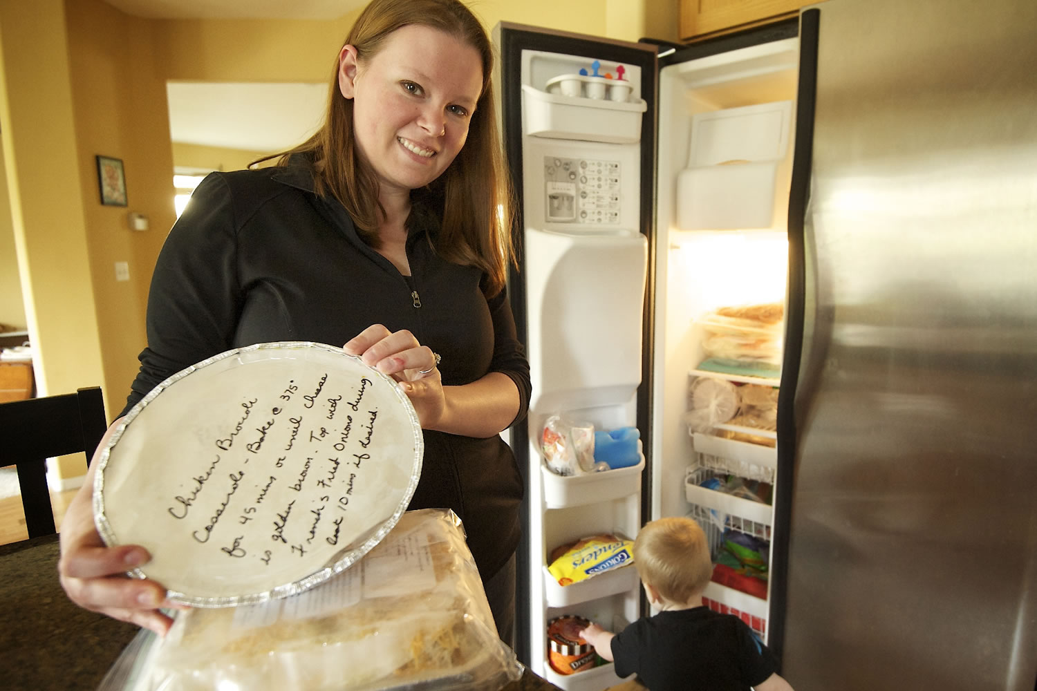 Julia Schetky shows off some of the meals she received at a moms group food swap last month, while her son, Ethan, checks out the other food in the freezer at the family home in Salmon Creek.