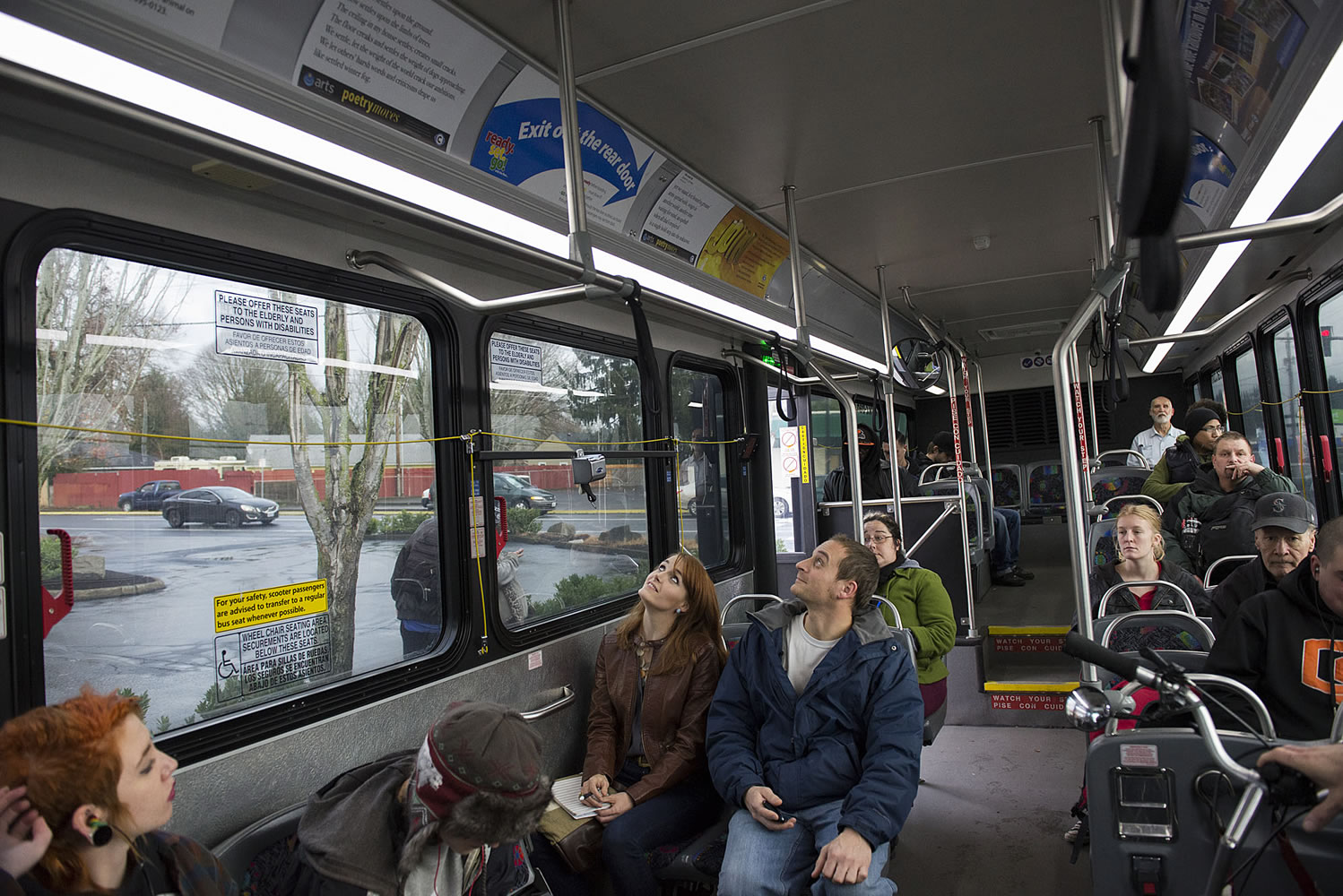 Poet Erin Iwata of Ridgefield, center in brown jacket, reads some moving poetry wtih Michael Atton of Vancouver aboard the no. 4 bus along Fourth Plain Boulevard on Dec. 14.