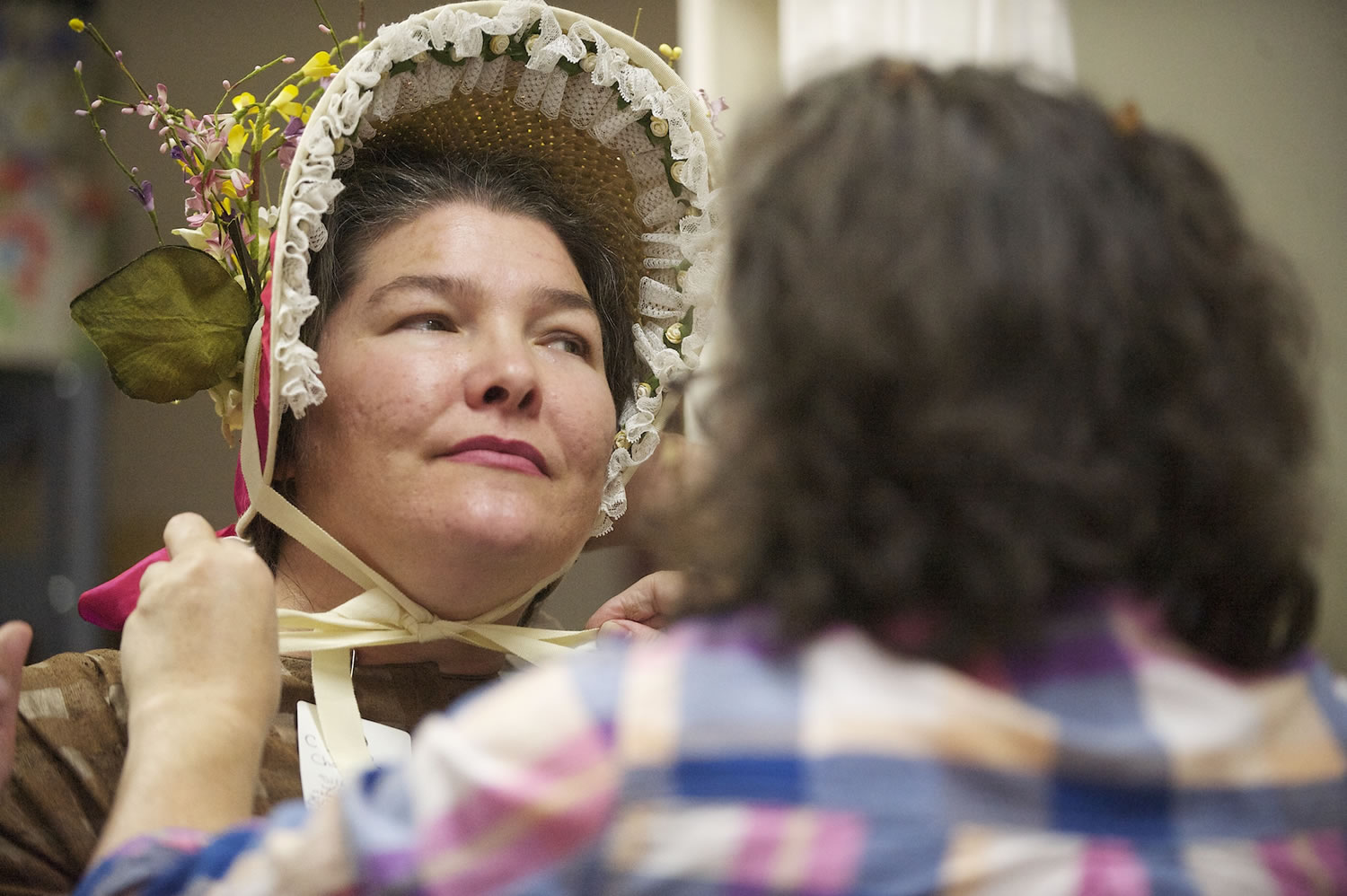 Heidi Pierson, left, holds still as Eileen Trestain, head of the costume department at the Fort Vancouver National Historic Site, checks out a bonnet Wednesday.